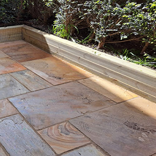 image of Indian Sandstone being laid with Decking Board used as a Planter / Border, this is an after image as part of an image slider