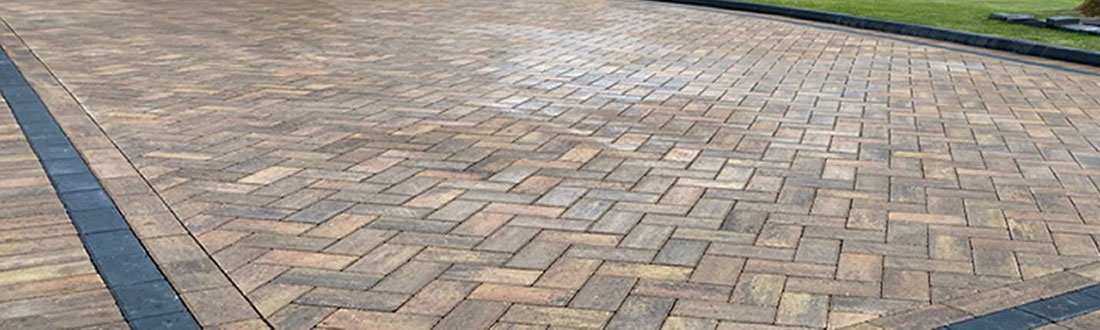 A wide shot of a driveway made of block paving stones in Newcastle upon Tyne. The driveway is surrounded by lush green grass and trees.