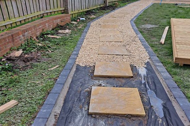 image of a Pathway being laid mid job, on the image we see the Breathable membrane, then the Charcoal Block Paving that we used as Edging stone or Border, then the Buff flagstones that compliment the whole look and feel of the design, this works our really well and looks striking but traditionally homely